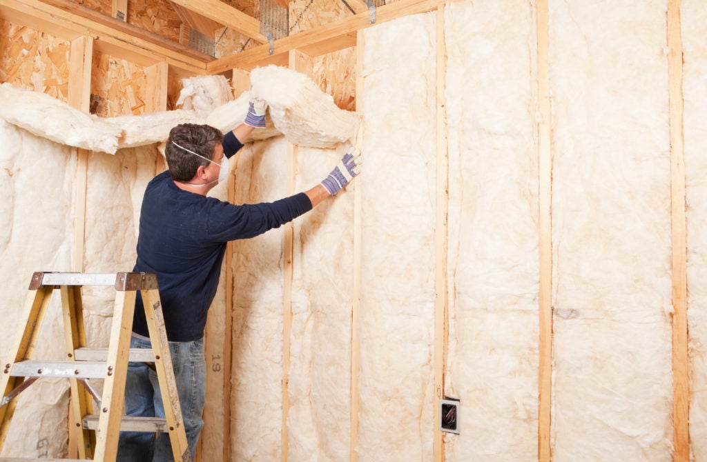 A man making a green home improvement by applying layers of insulation to his walls 