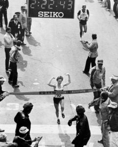 As a young adult, Joan Benoit Samuelson crosses the finish line with her arms raised in excitement. 