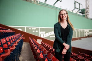 A woman standing in the stands at Fenway park in view of the Green Monster