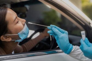  A woman receiving a COVID-19 test from her car, provider with gloved hands holds a testing swab