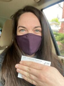 A woman wearing a mask holding a COVID-19 vaccination card