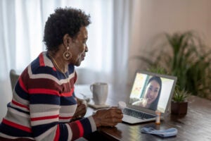 African American woman sitting at her dining room table speaking with her general practitioner via video call.