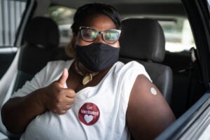 Portrait of a happy woman in a car with a 'get vaccinated' sticker - wearing face mask
