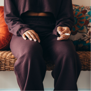 A person who is sitting on a couch holding a joint, wearing brown loungewear