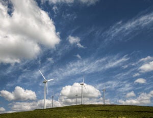 Wind farm on a green hill under a blue sky dotted with white clouds