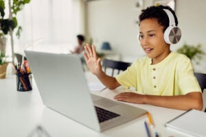 Smiling black boy making video call over laptop and waving while e-learning at home.