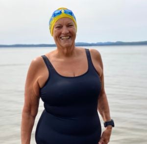 Gallant-Charette poses in front of Sebago Lake wearing a navy full-piece bathing suit, yellow bathing cap, and blue goggles. 