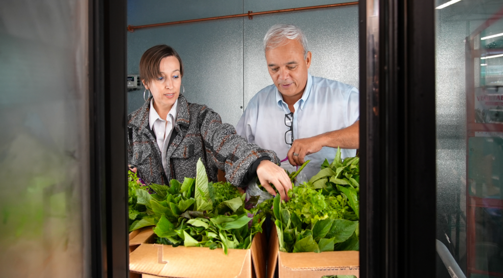 John Santos and a co-op employee sort through green produce in front of the co-op's refrigerator