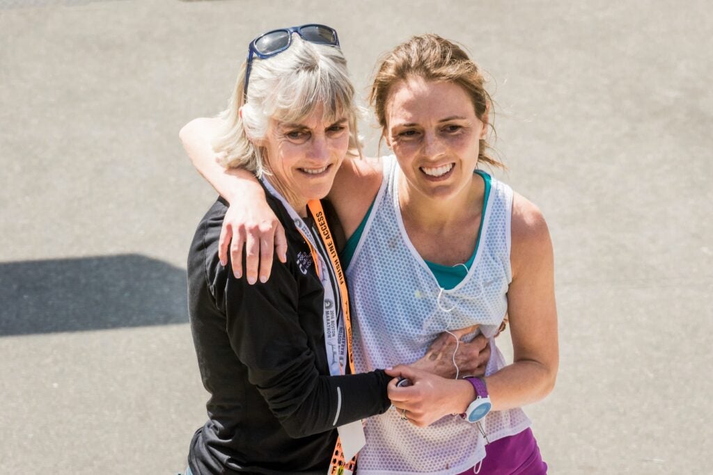 A mother and adult daughter embrace and lean on each other after running a race