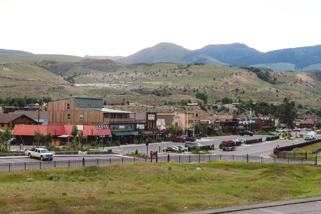 A strip of store fronts with a parking lot in front of it and rolling hills behind it.