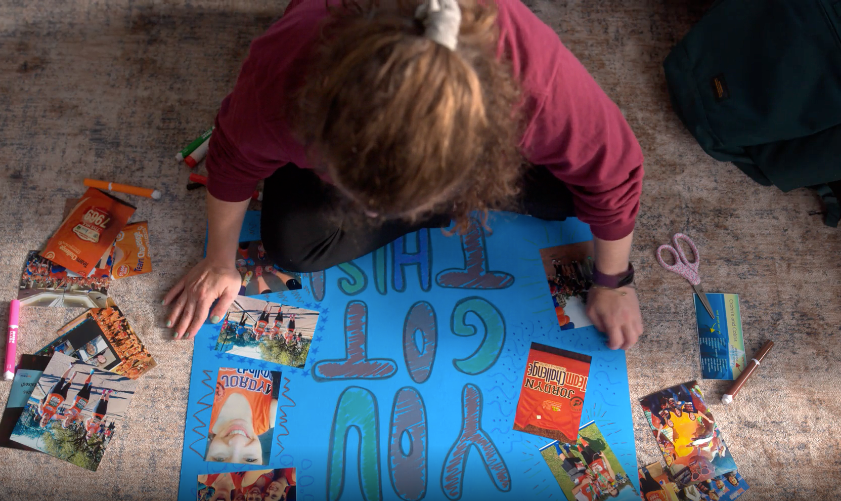 An overhead shot of a woman putting together a poster that reads "YOU GOT THIS!" with glued on pictures surrounding it. 