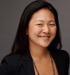 Headshot of a smiling Asian woman wearing a blazer and a necklace.