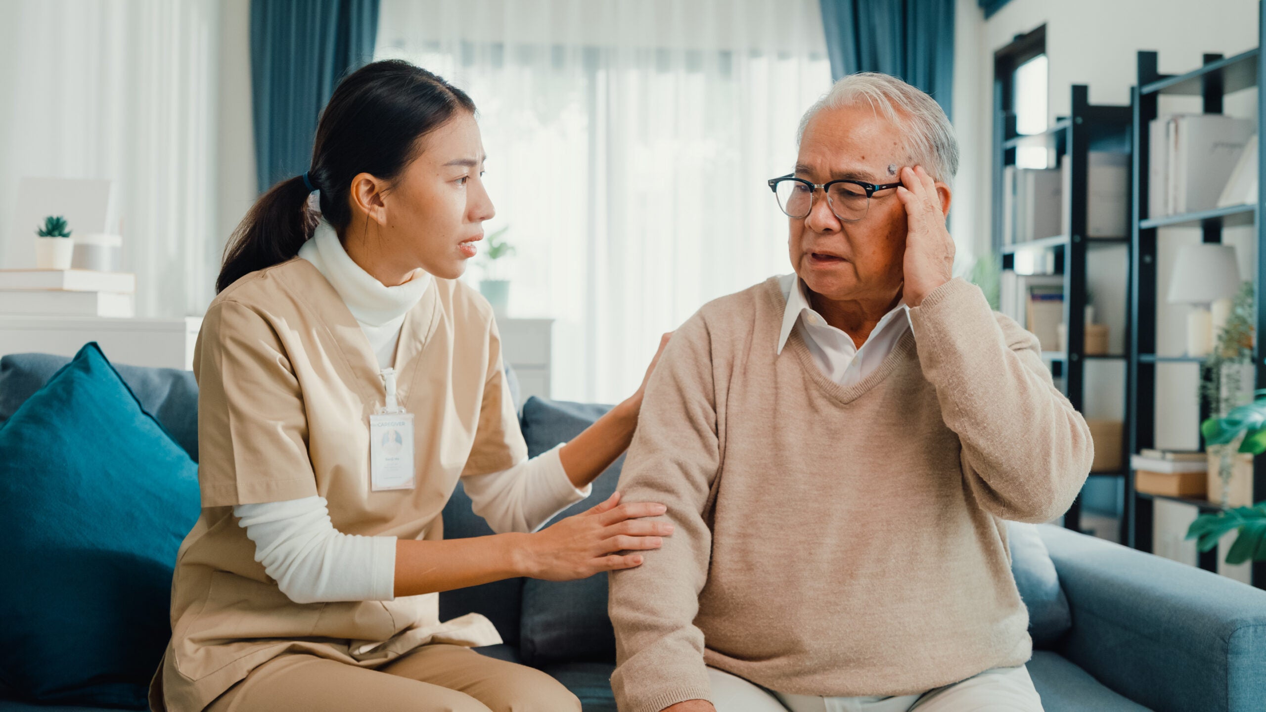 Asian physician wearing beige scrubs consoling her elderly Asian patient
