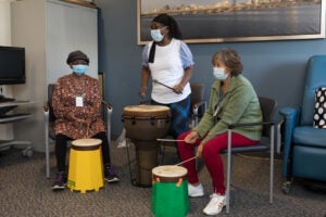 A group of elderly women sit in a drum circle with big and colorful drums
