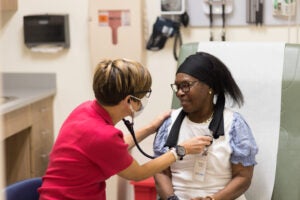 An elderly Black woman has her heart checked by a short haired nurse