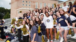 A large group of girls with pom poms and school colors pose outdoors on stairs.