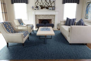 A spacious living room a blue rug and blue accents on the off-white chairs, sofa, and coffee table in front of a large fireplace.