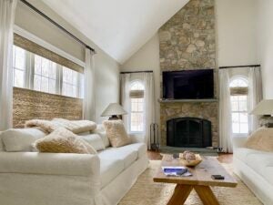 A cozy and clean living room with a white couch and stone fire place.