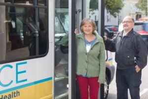 An elderly Asian woman stands in front of a bus she is about to board