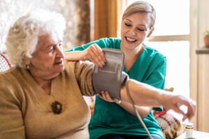 A female nurse measures senior woman's blood pressure at home.