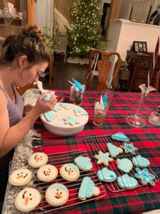 A woman sitting in a dining room decorated for Christmas frosts snow themed sugar cookies