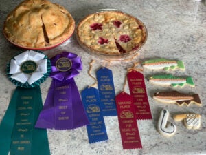Two pies and an assortment of cookies sit on a counter with many county fair award ribbons next to them