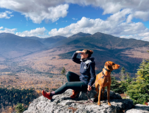 Woman sitting at viewpoint with dog looking at White Mounatins, NH