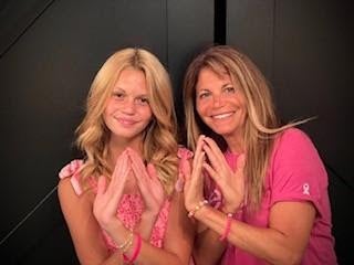 Blond mother and daughter wearing pink shirts and doing ribbon hand gesture 