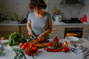 A middle aged woman in her kitchen slices peppers and tomatoes 