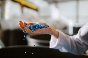A hand holds out a pile of pellets made of biodegradable materials with some slipping through its fingers
