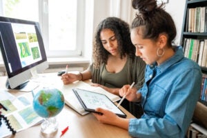 Two young woman sit at a desk with a computer and tablet preparing concepts for climate protection