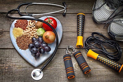 Fruits and nuts on cutting board surrounded by stethoscope and jump rope. 