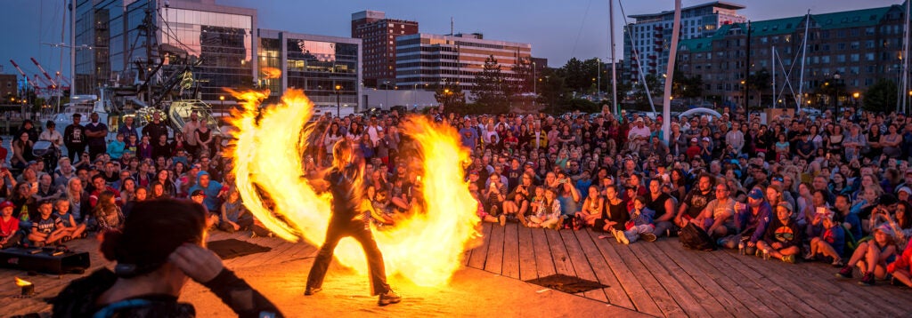 A flame thrower performs outside for a huge crowd of seated people. 