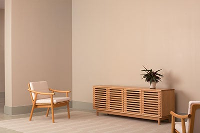 Wooden chairs with white cushions in pale peach room with wooden credenza. Atop the credenza sits a potted plant.