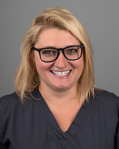 Young blond nurse with rectangular black framed glasses smiling genuinely.