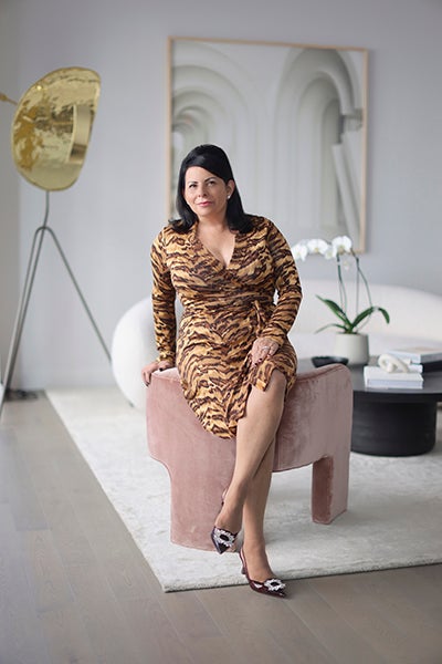 Woman in leopard print wrap sitting on the back edge of pale pink crushed velvet chair. 