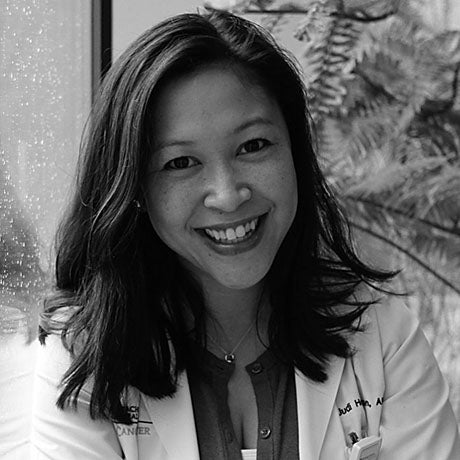 Black and white portrait of smiling black-haired nurse in front of fern. 