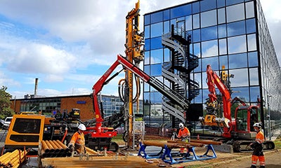 Construction site with red crane in front of reflective building and spiral structure.