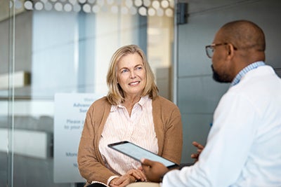 Senior woman with blond hair talking and listening to a male medical professional in a hospital. 