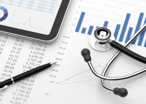 Black and silver stethoscope sitting on top of a desk of financial statements and charts. 