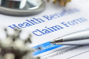 Close-up image of a silver pen and stethoscope sitting on top of a health benefits claim form