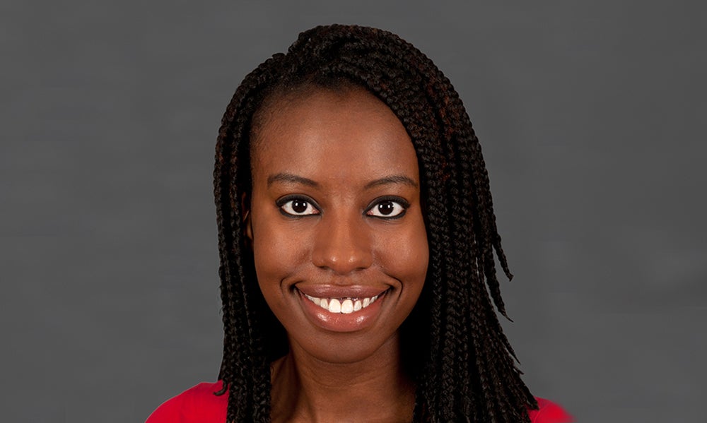 Amara Anosike, an adult woman with braided hair smiling and wearing a red top