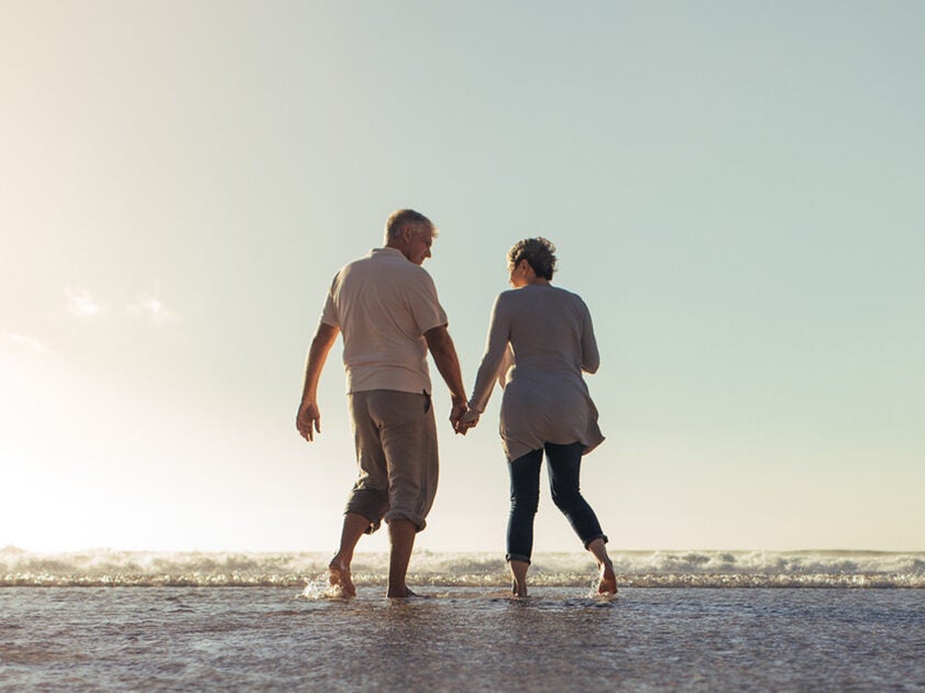 Shot of a happy mature couple holding hands and walking on the beach during sunset.