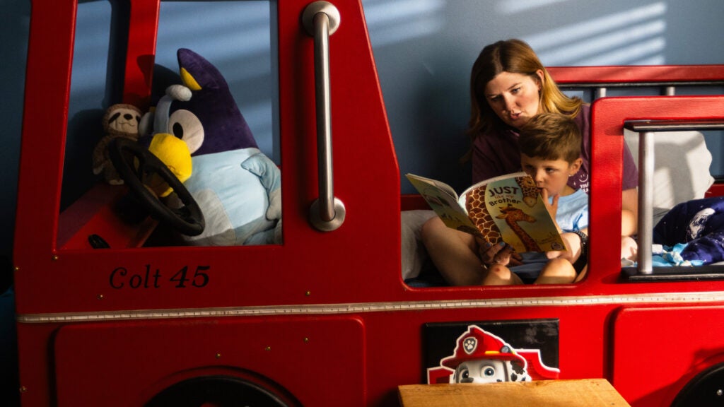 Kelsey reads to her son, Colt, in his bed, which resembles a red fire truck. Inside, there are stuffed animals. 