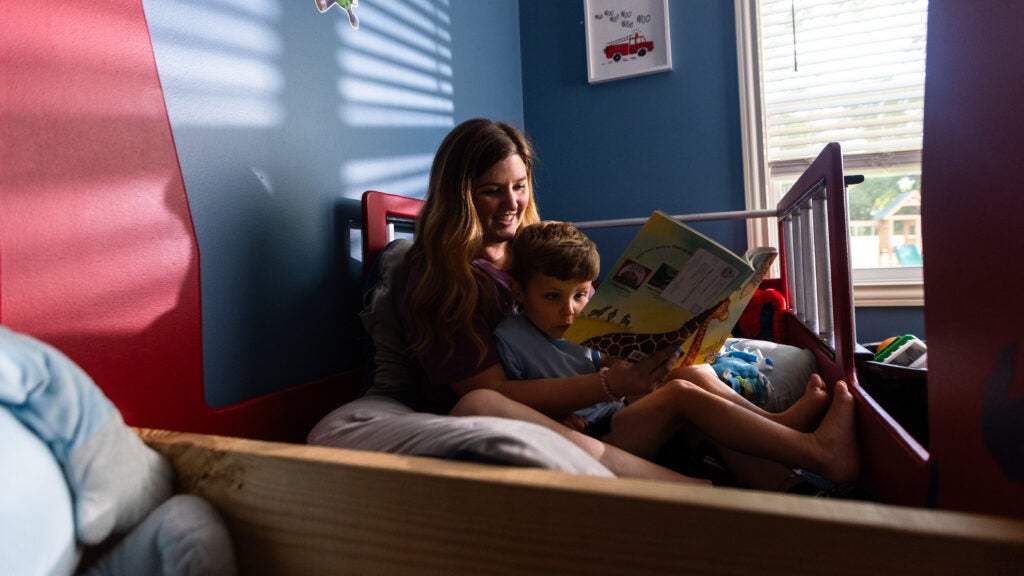 Kelsey Coleman sits in bed with her son, Colt, reading a children's book. Colt looks surprised at its contents while Kelsey smiles.