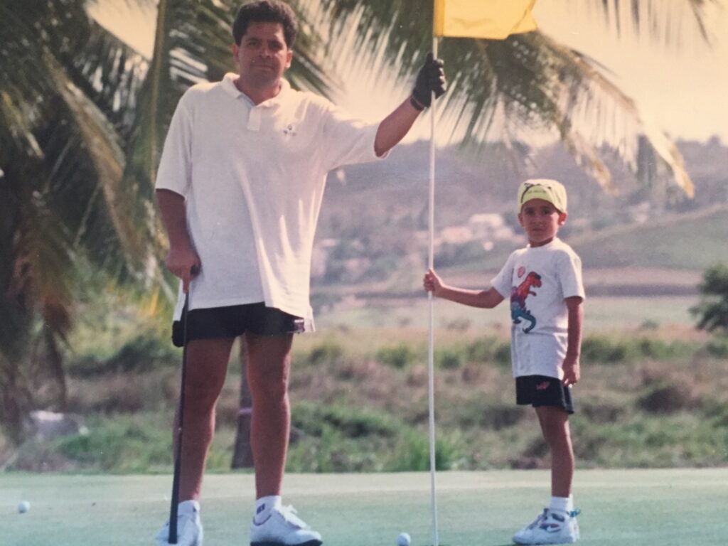 30-year-old image of Tony Gallardo and his young son posing on a golf course while holding a yellow flag. 