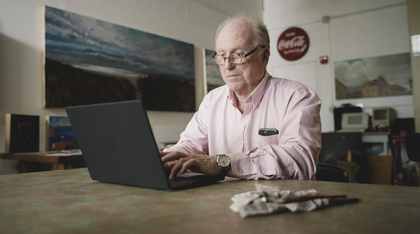 Older man typing on laptop in his art studio