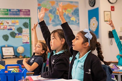 Three school girls raising their hands in class.