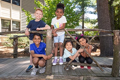 Five diverse children smiling in front of a wooden gate.
