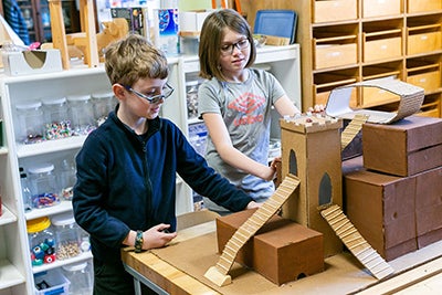Two young children building a castle out of cardboard at school. 